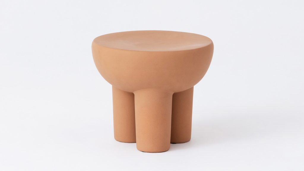 A small, round, terracotta-colored stool with a smooth surface and four thick cylindrical legs, photographed against a plain white background.