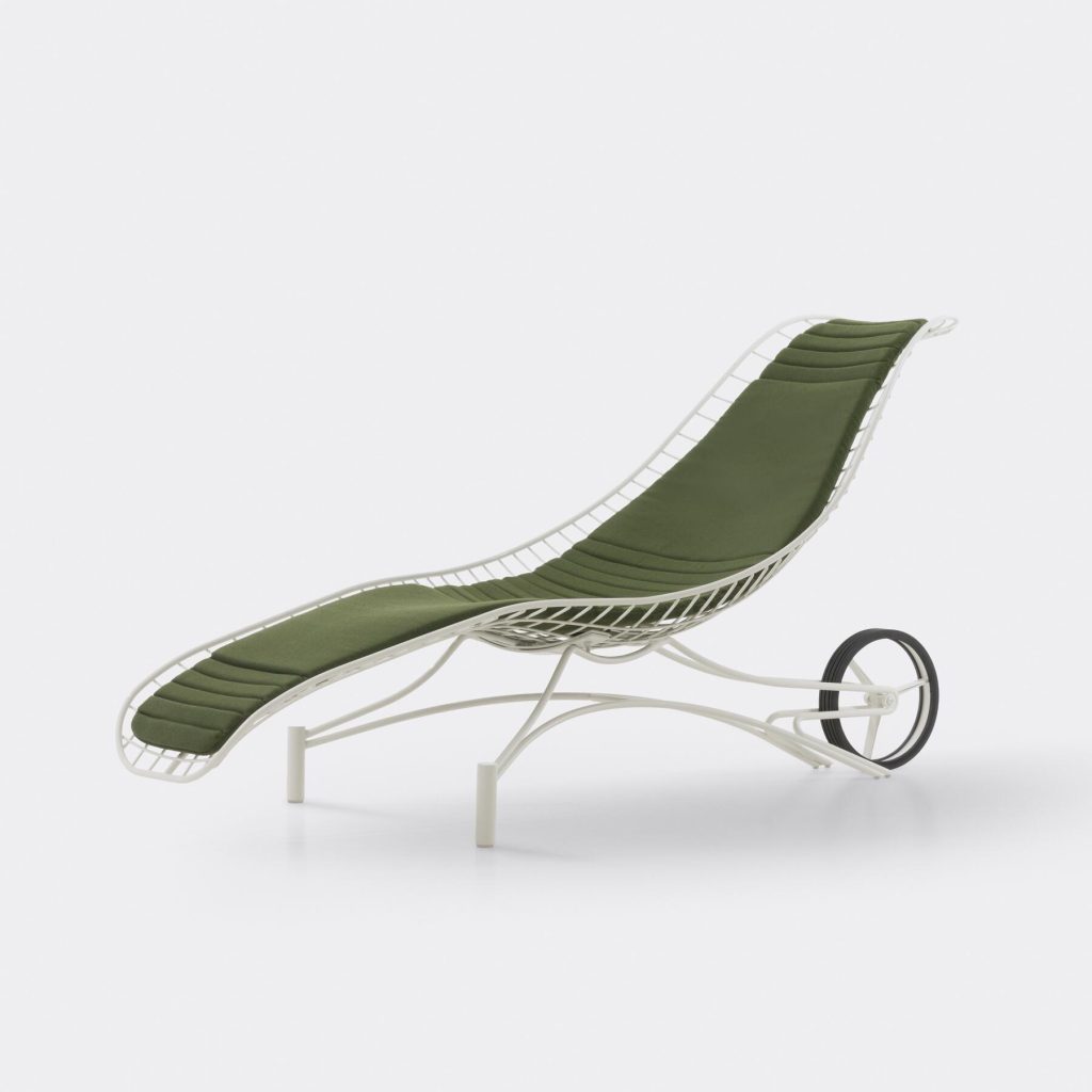 A modern lounge chair with a white metal frame and curved green cushioned seat, featuring two large back wheels for mobility, set against a plain white background.