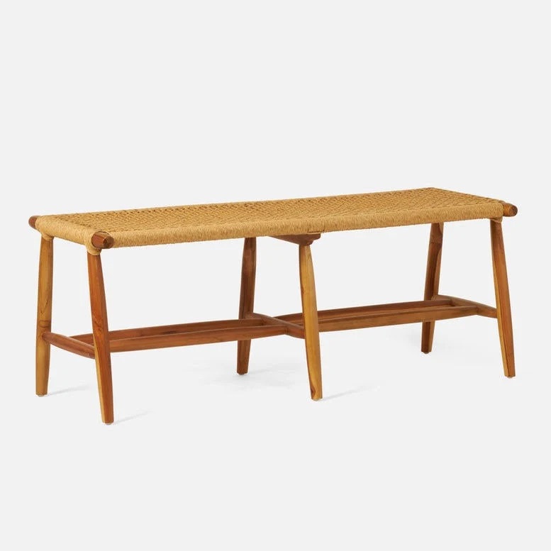 A wooden bench with a woven rattan seat, featuring angled legs and a minimalist, natural design. The bench has a support bar connecting the legs.
